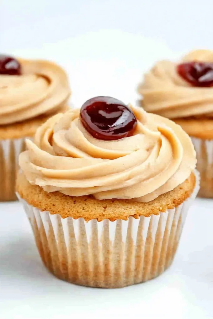 Three cupcakes in white liners topped with creamy swirls and a dollop of jelly.