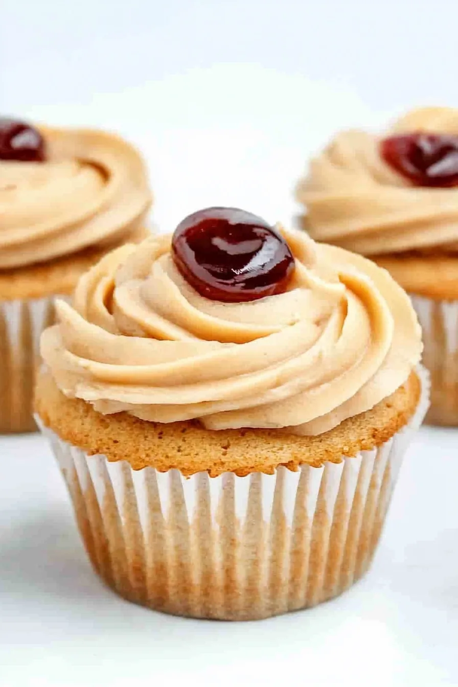 Three cupcakes in white liners topped with creamy swirls and a dollop of jelly.