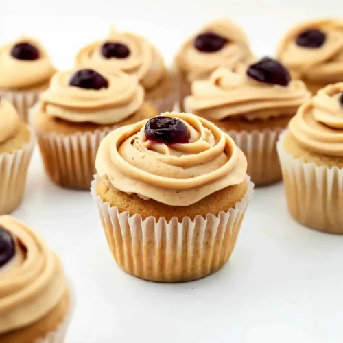 Golden cupcakes finished with smooth frosting and vibrant red jam accent.