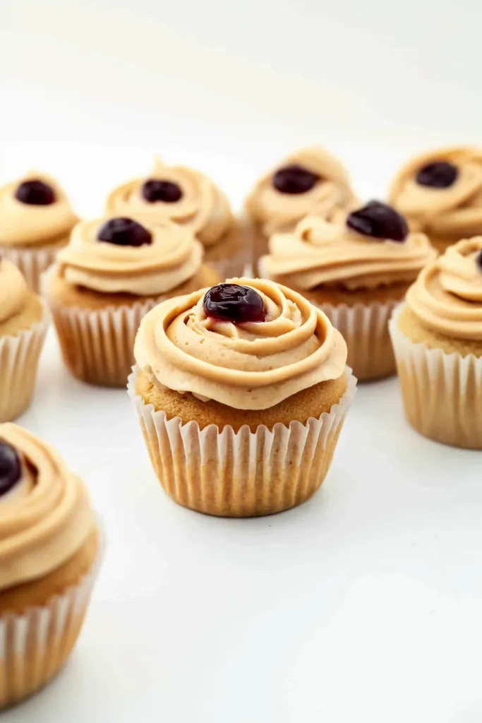 Golden cupcakes finished with smooth frosting and vibrant red jam accent.