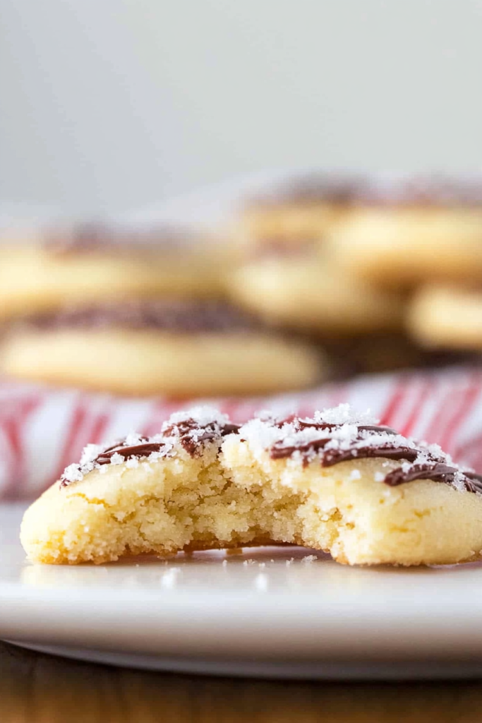 Soft golden cookie with a bite taken, drizzled in chocolate and sprinkled with sugar.