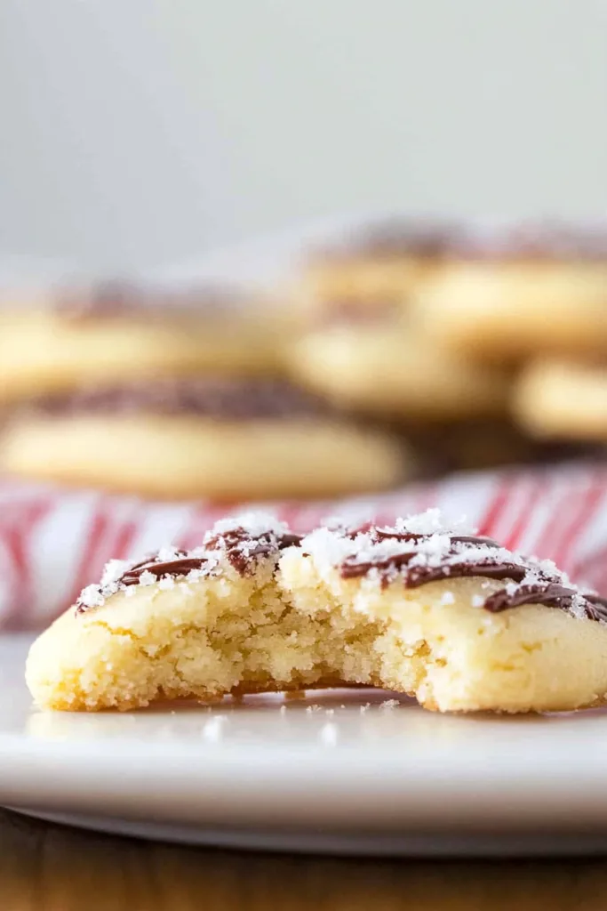 Soft golden cookie with a bite taken, drizzled in chocolate and sprinkled with sugar.