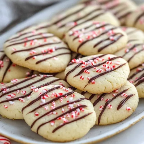 Plate of holiday cookies decorated with thin chocolate lines and peppermint bits.
