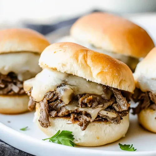 Closeโup of mini cheesesteak sandwiches with gooey cheese and tender steak tucked inside soft rolls.