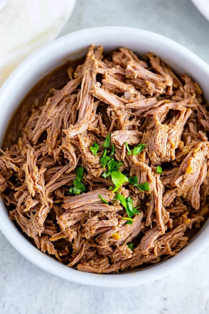 Savory shredded beef with visible fibers and a sprinkle of parsley.