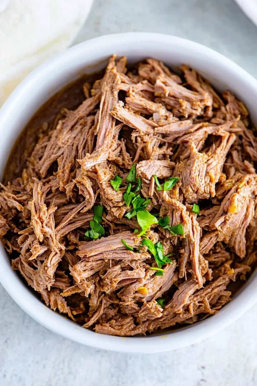 Savory shredded beef with visible fibers and a sprinkle of parsley.