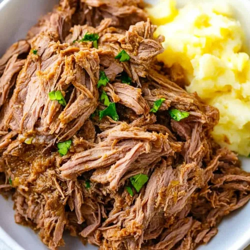 Rich brown beef strands plated alongside smooth mashed potatoes.