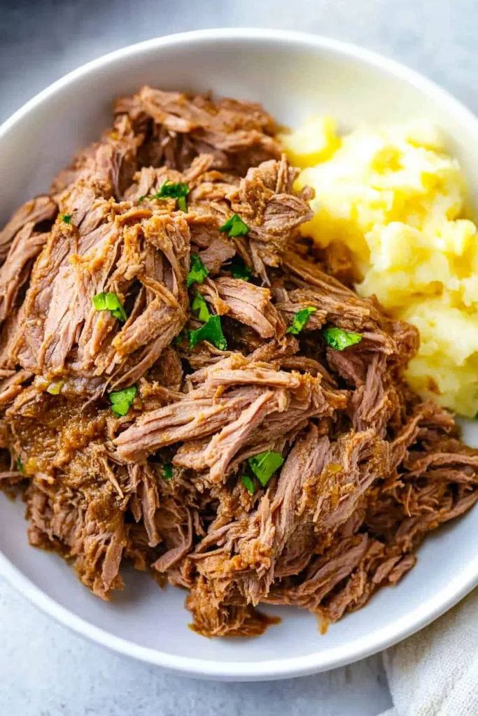 Rich brown beef strands plated alongside smooth mashed potatoes.