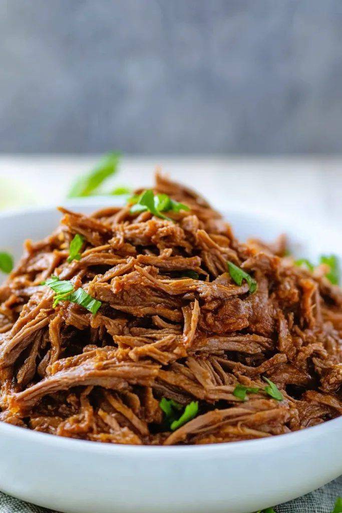 Close-up of moist, slow-cooked beef garnished with fresh herbs.