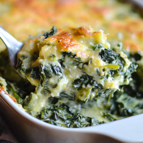 Golden baked casserole with creamy spinach layers lifted by a spoon