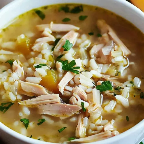 Freshly prepared comfort food soup with shredded turkey pieces, rice, aromatic vegetables, and parsley garnish.