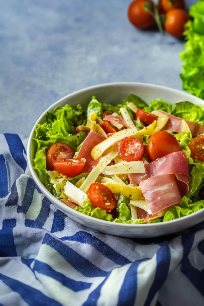 Fresh lettuce tossed with ham, cheese strips, and cherry tomatoes in a white bowl.