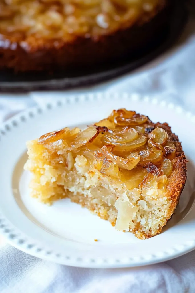 Slice of golden cake topped with glossy caramelized onions on a white plate.
