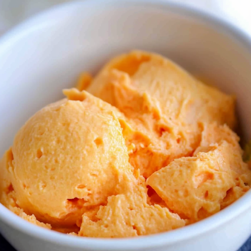 Scoops of creamy orange salad served in a white bowl.