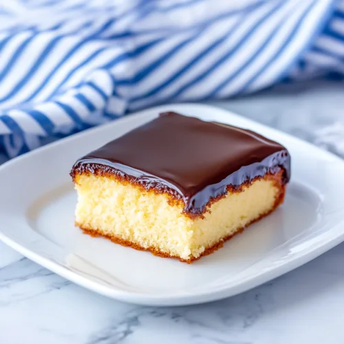 Slice of yellow cake topped with glossy chocolate frosting.