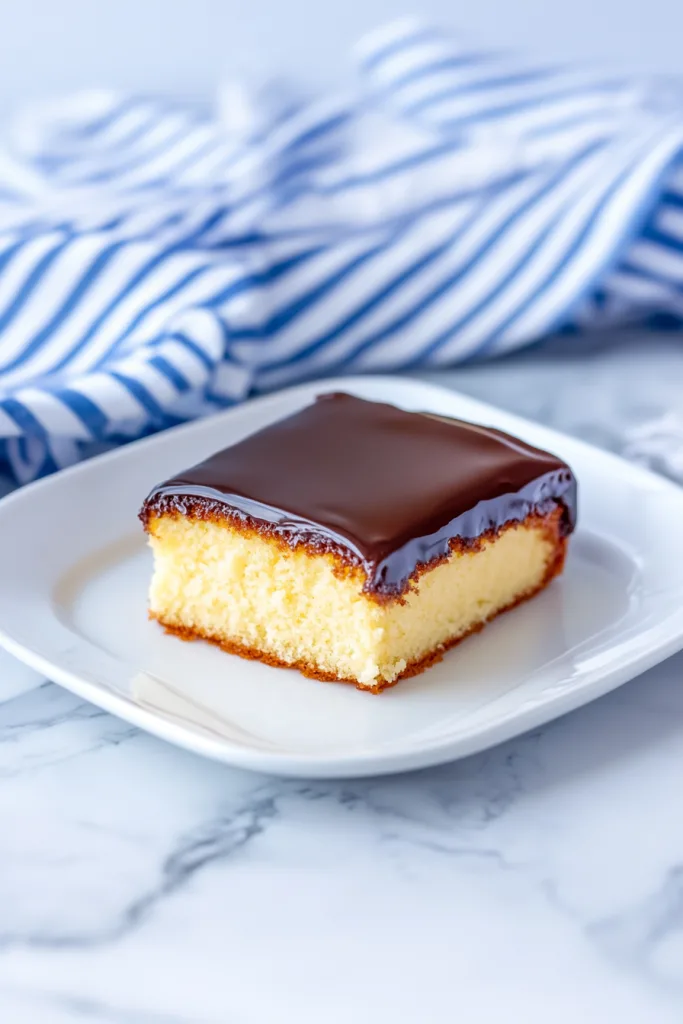 Slice of yellow cake topped with glossy chocolate frosting.