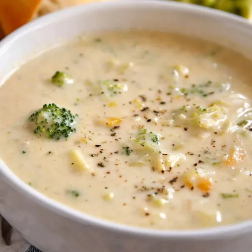 Creamy soup with broccoli florets and diced carrots in a white bowl.