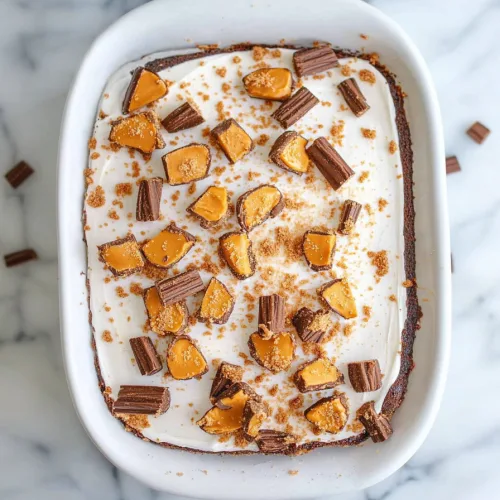 A rectangular cake topped with smooth frosting, caramel drizzle, and chopped candy pieces on a white plate.