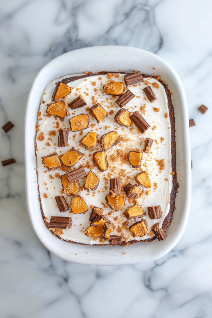 A rectangular cake topped with smooth frosting, caramel drizzle, and chopped candy pieces on a white plate.