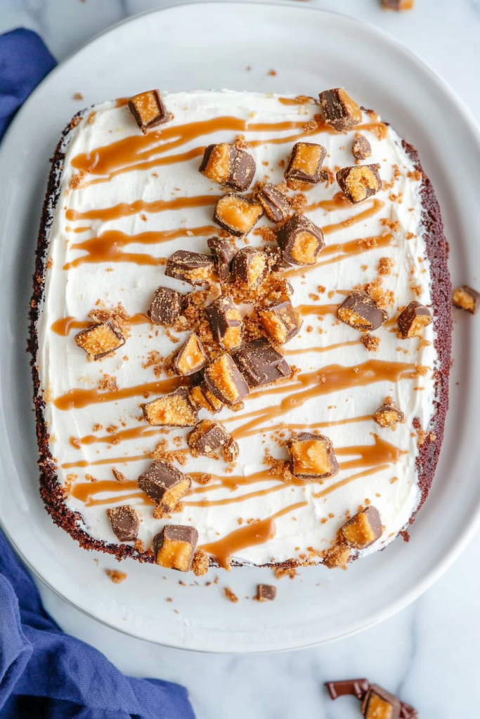 Overhead view of a dessert with creamy white icing, caramel ribbons, and crunchy candy bar topping.