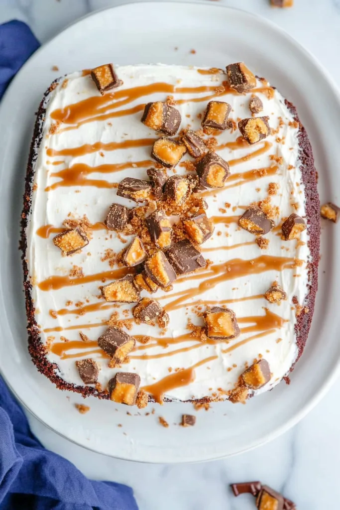 Overhead view of a dessert with creamy white icing, caramel ribbons, and crunchy candy bar topping.
