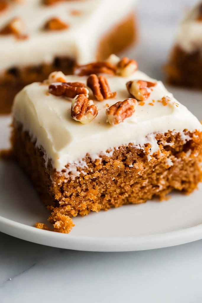 Moist brown cake slice topped with creamy frosting and pecans.