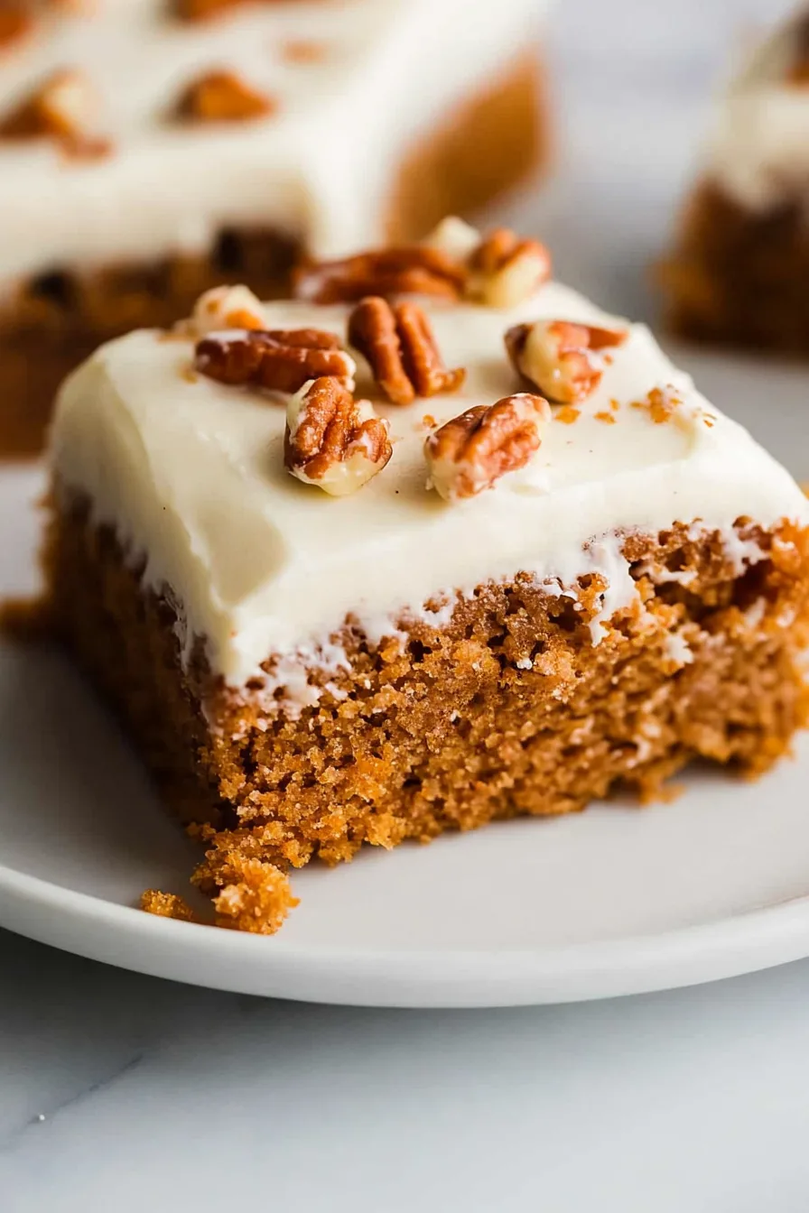 Moist brown cake slice topped with creamy frosting and pecans.
