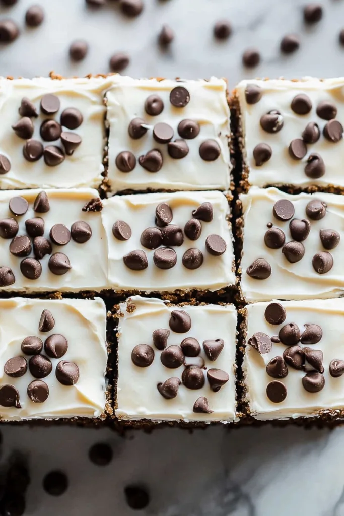 Neatly arranged dessert bars with smooth frosting and scattered chocolate chips.