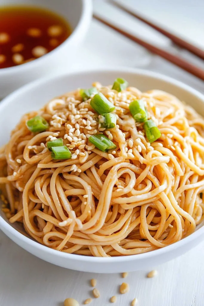 Bowl of noodles topped with sesame seeds and chopped green onions.