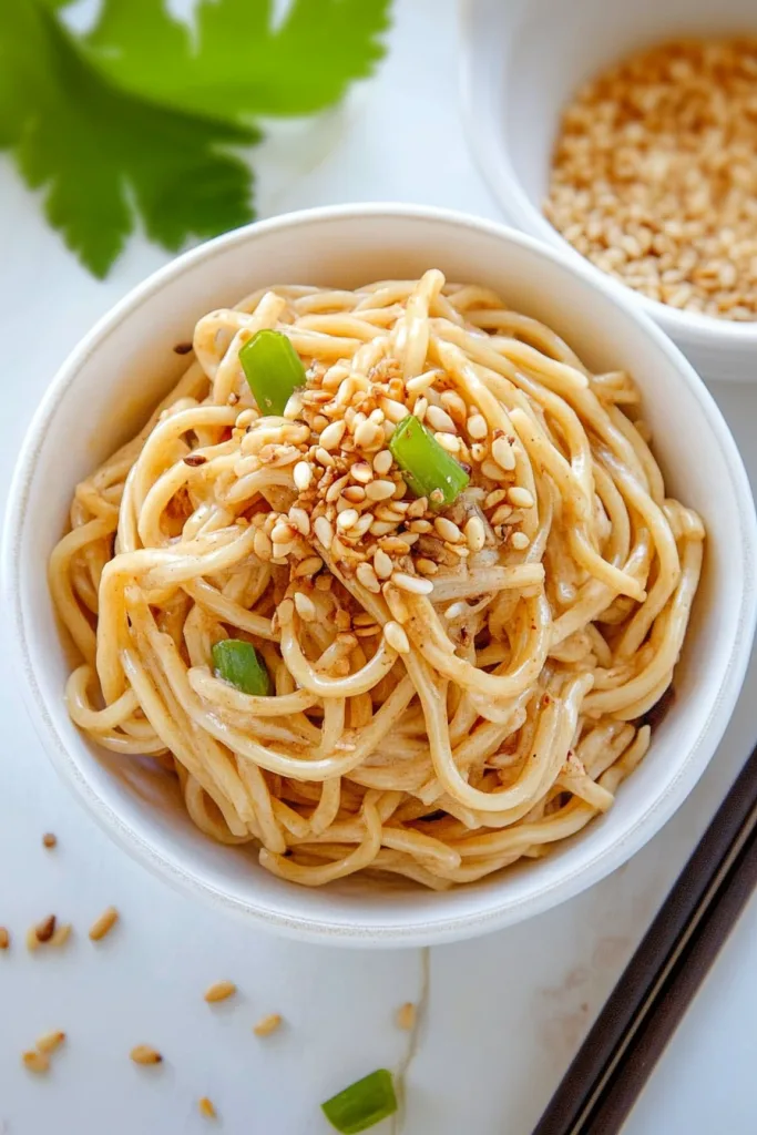 Overhead view of noodles coated in light sauce, served with chopsticks nearby.