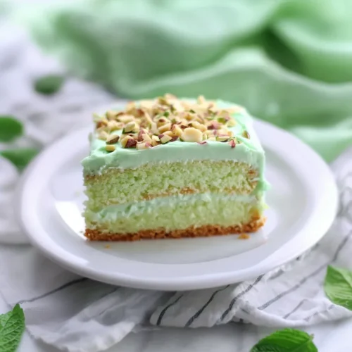 Slice of light sponge cake topped with pale green frosting and chopped pistachios.