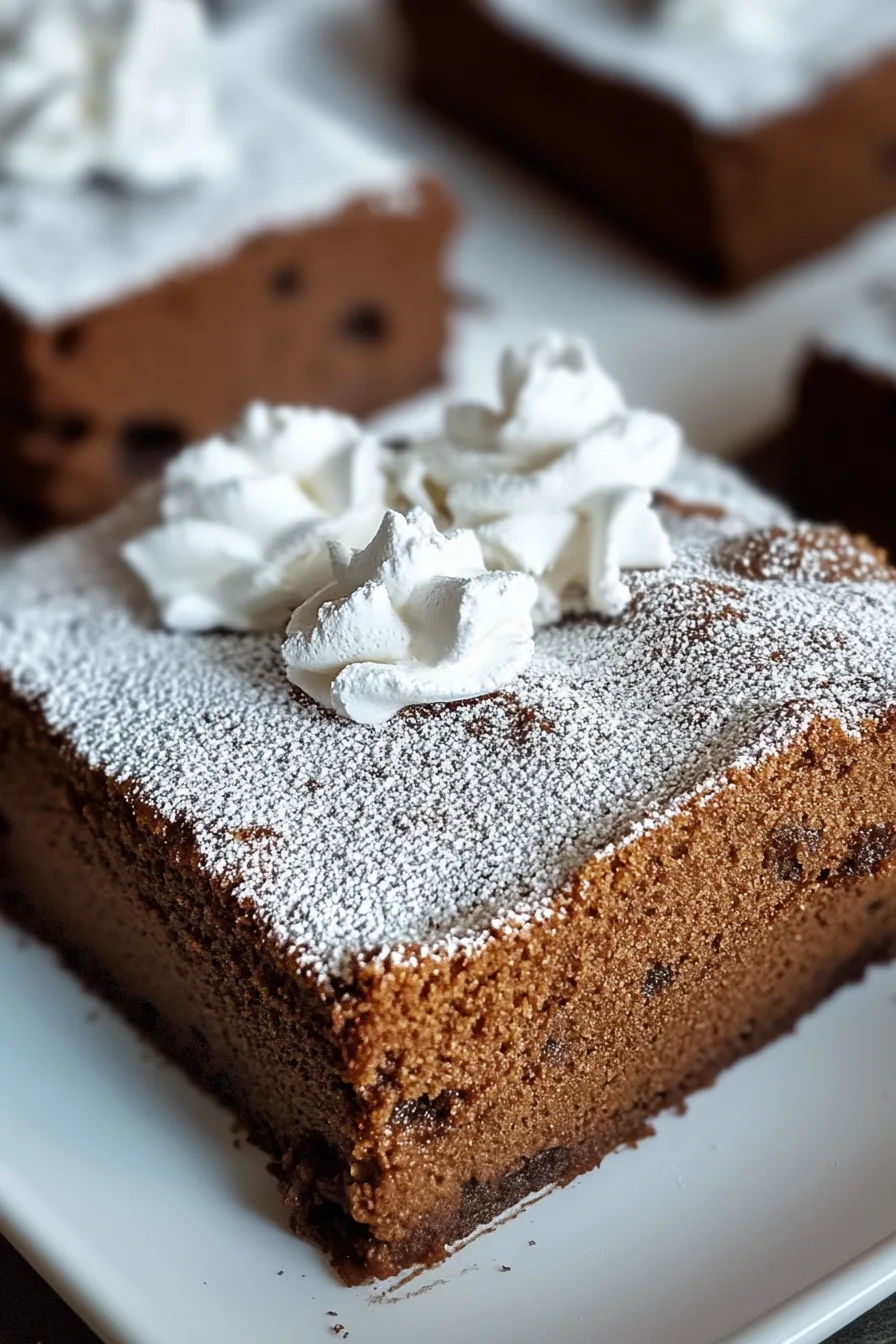 Square slice of spiced cake dusted with powdered sugar and topped with whipped cream.