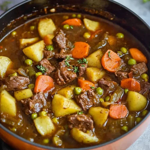 Chunky beef and vegetable stew served in a pot with herbs.