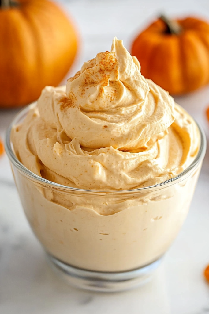 A glass bowl filled with fluffy orange whipped cream, topped with a light dusting of spice.