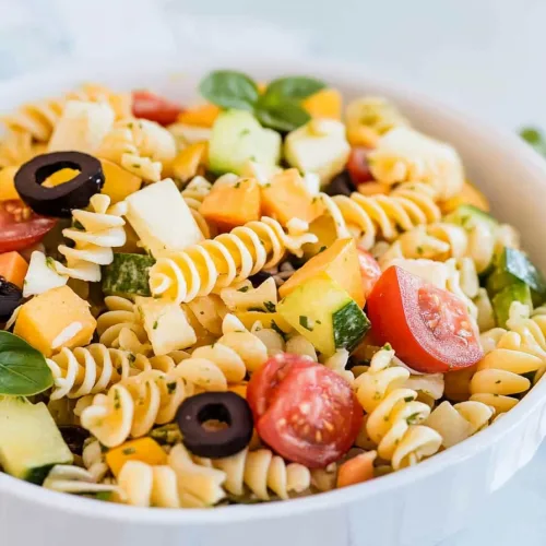 White bowl filled with vibrant pasta and crisp cucumber pieces.