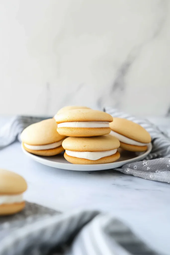 Plate of golden sandwich cookies filled with creamy white frosting.