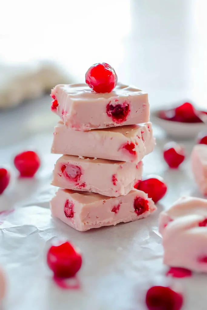Final shot of pale pink fudge cubes with vibrant cherries scattered around.