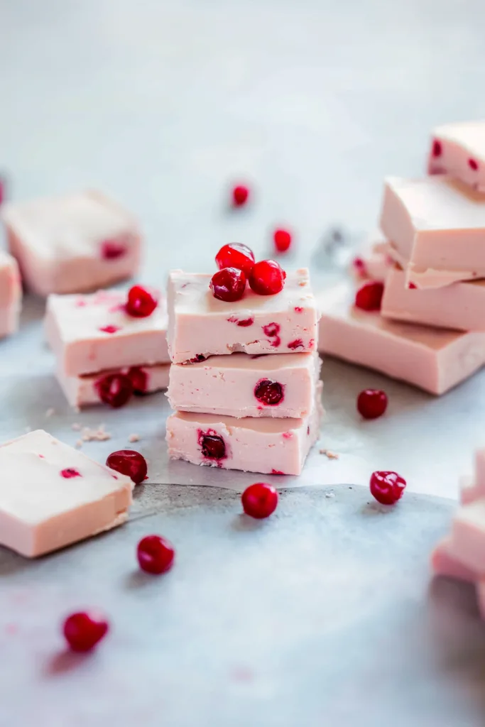 Stacked pieces of creamy pink fudge with glossy cherries on top.