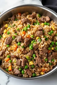 A close-up of a bowl filled with golden fried rice, tender beef slices, peas, and carrots.