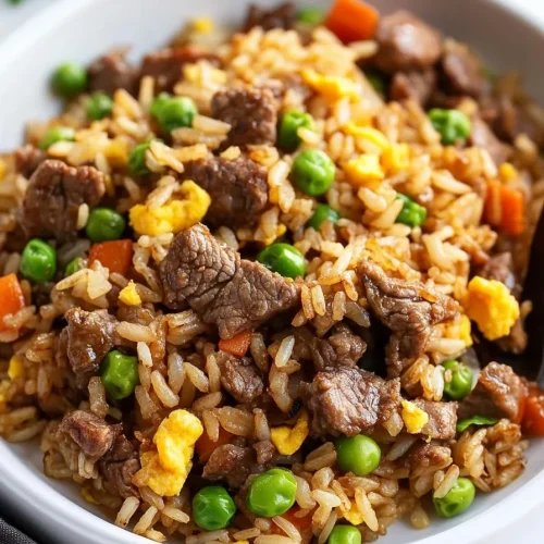 Freshly cooked rice stir-fried with beef, egg, and vegetables, served in a white dish.