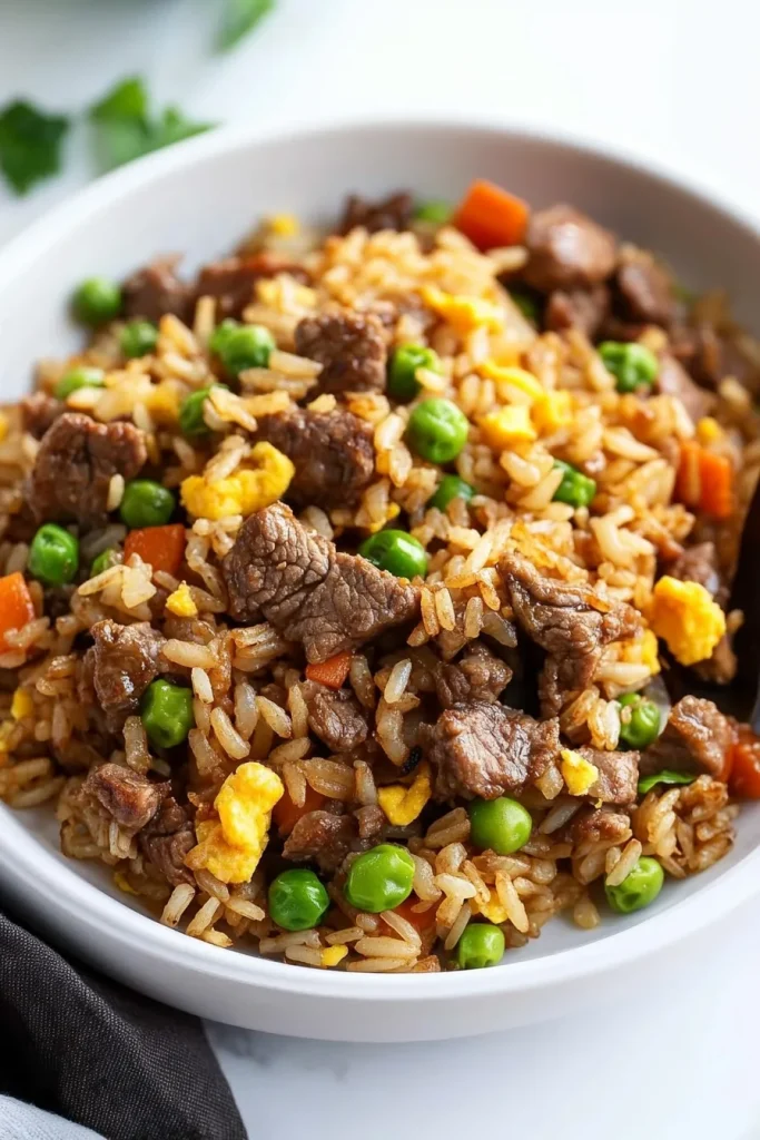 Freshly cooked rice stir-fried with beef, egg, and vegetables, served in a white dish.