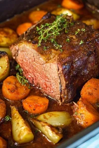 Juicy beef roast nestled among roasted carrots and parsnips, topped with sprigs of thyme.