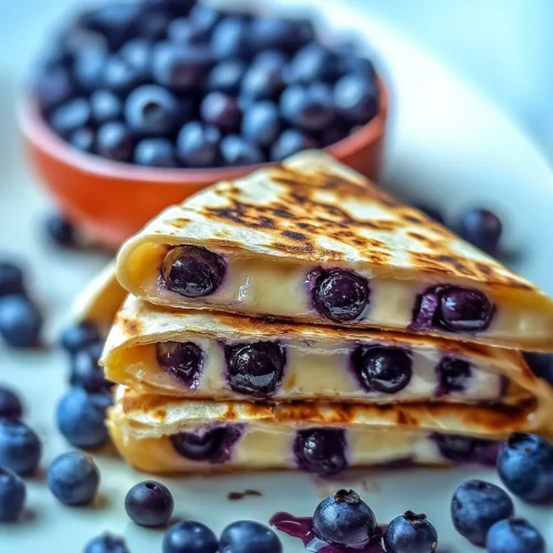 Crispy folded flatbread showing a blueberry and cream filling, with a bowl of berries in the background.