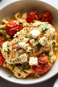 Close-up of baked chicken topped with crumbled cheese and fresh herbs.
