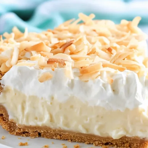 Slice of pie with creamy coconut filling, topped with whipped cream and toasted flakes.