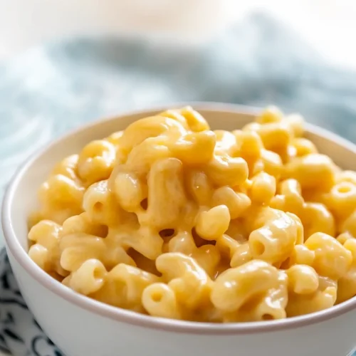 A white bowl filled with creamy macaroni coated in golden cheese sauce, resting on a patterned cloth.