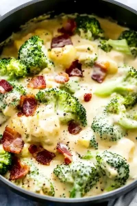 Close-up of thick, golden cheese soup dotted with green broccoli and garnished with bacon.