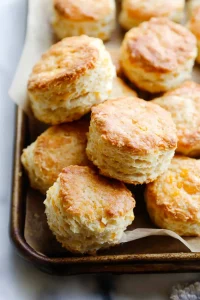 Golden-brown biscuits with flaky layers on a parchment-lined tray.