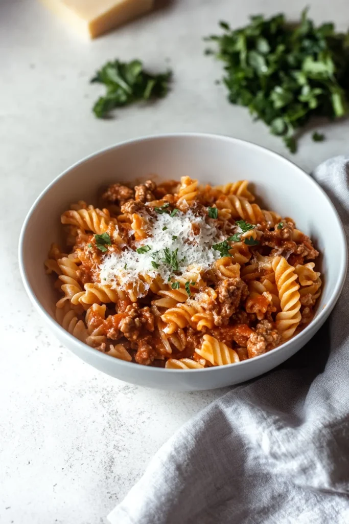 A hearty bowl of rotini pasta topped with rich tomato meat sauce, melted cheese, and fresh basil.