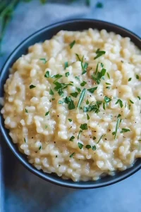 Freshly prepared risotto with a glossy surface, Parmesan shavings, and scattered herbs.